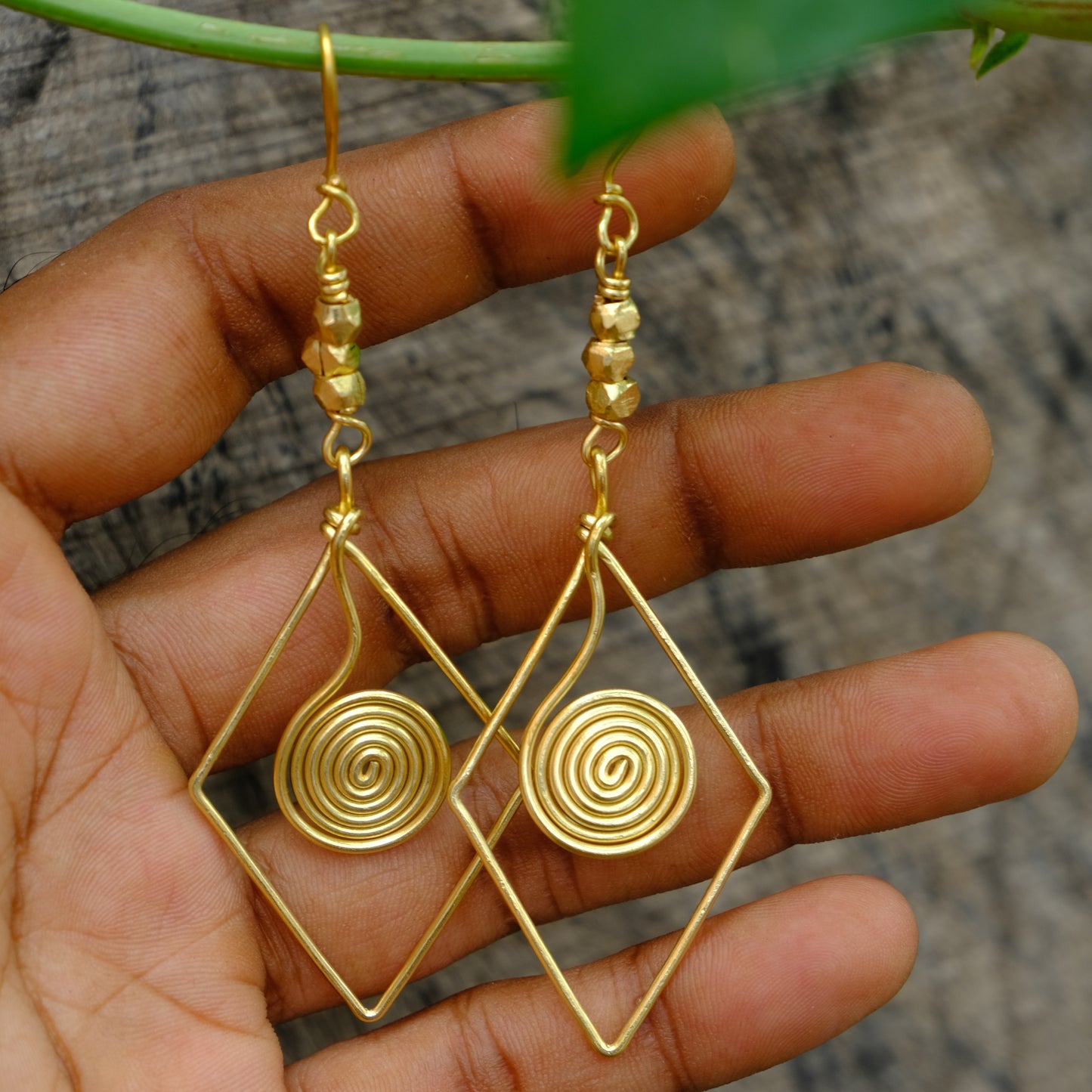Gold wire-wrapped spiral Dhokra Earring held in a hand with a blurred background