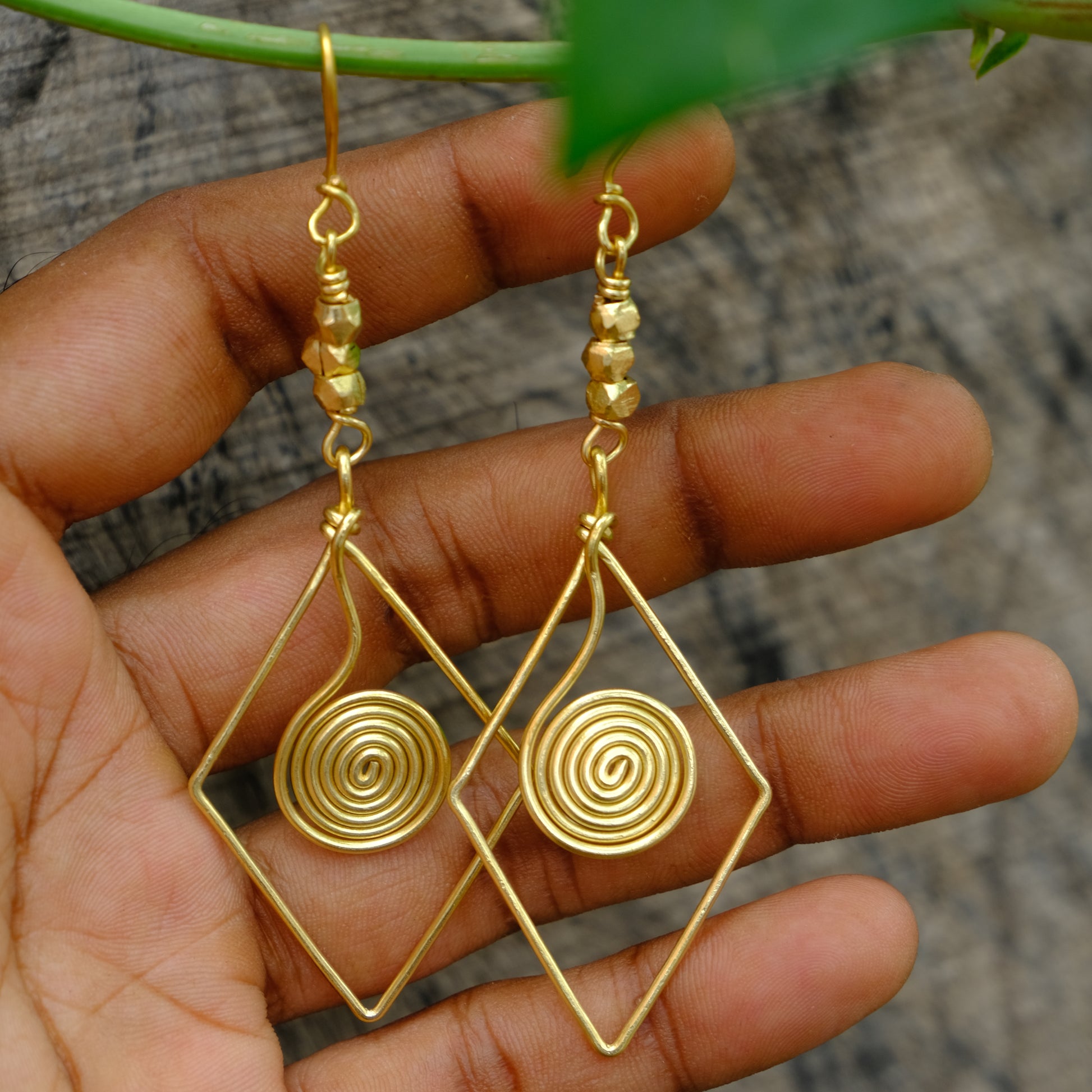 Gold wire-wrapped spiral Dhokra Earring held in a hand with a blurred background