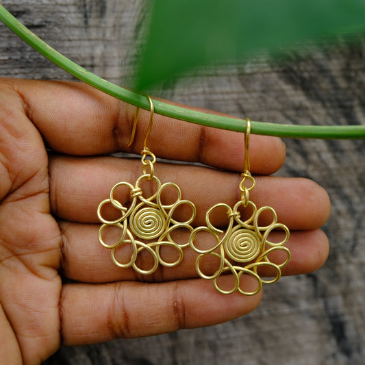 Gold Dhokra floral earrings held in a hand with a natural background