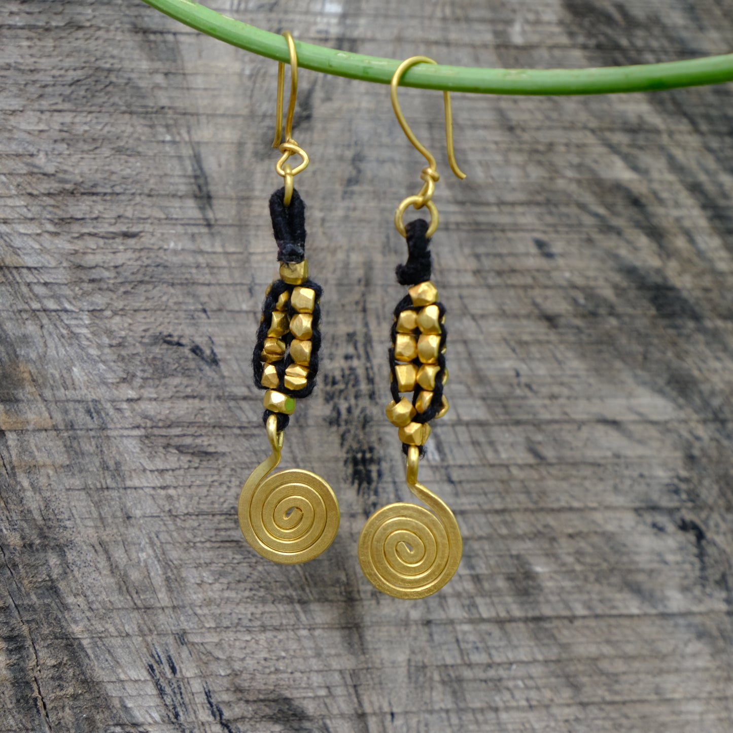 Gold spiral Dhokra earrings with black accents on a wooden surface