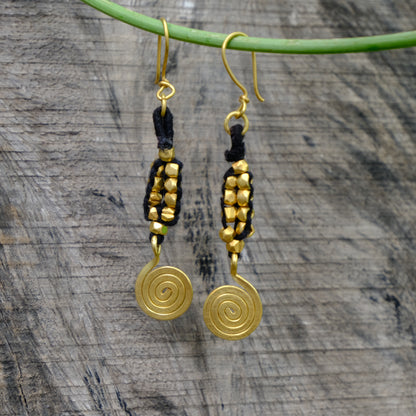 Gold spiral Dhokra earrings with black accents on a wooden surface