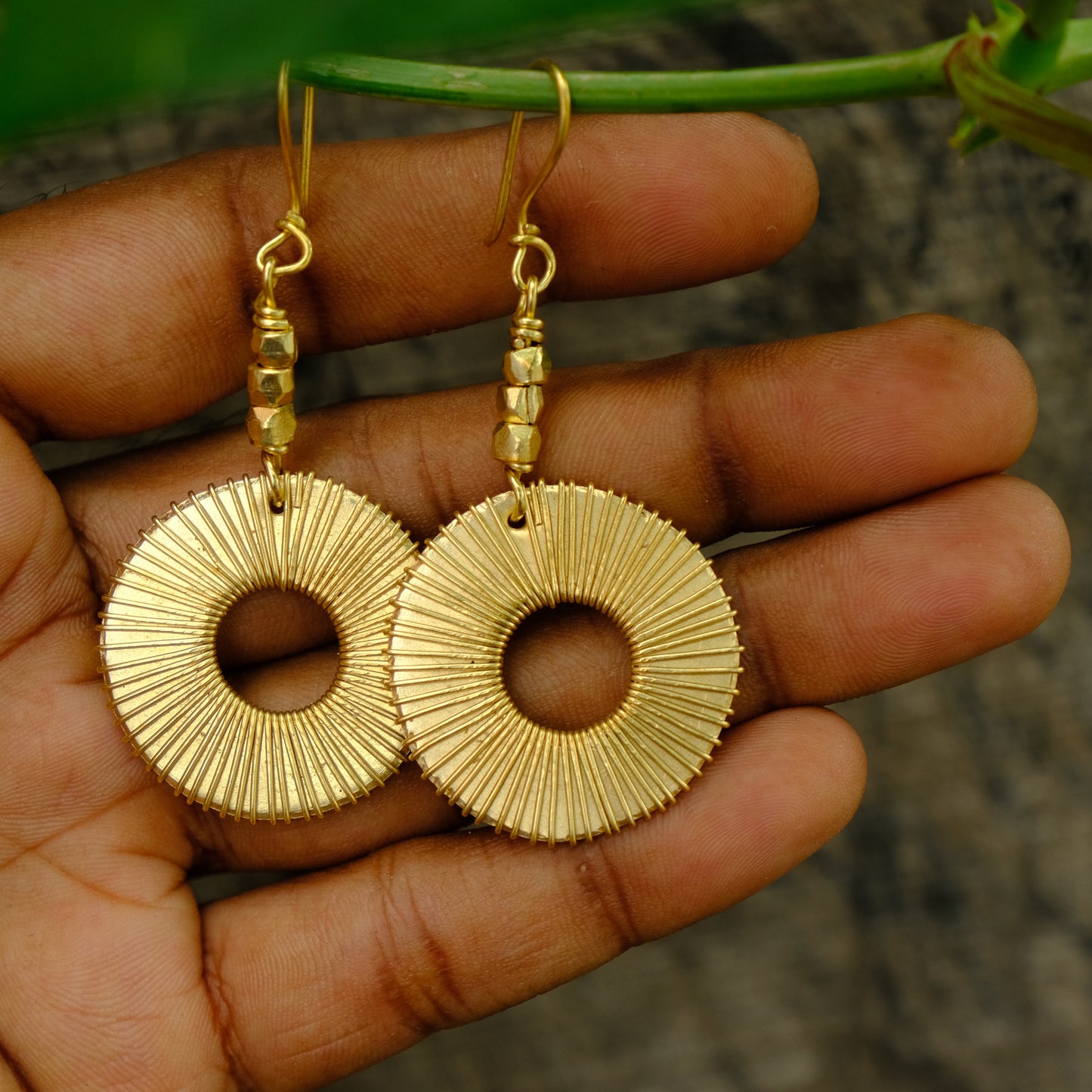 Gold Dhokra earrings held in a hand with a natural background
