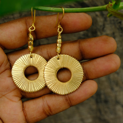 Gold Dhokra earrings held in a hand with a natural background