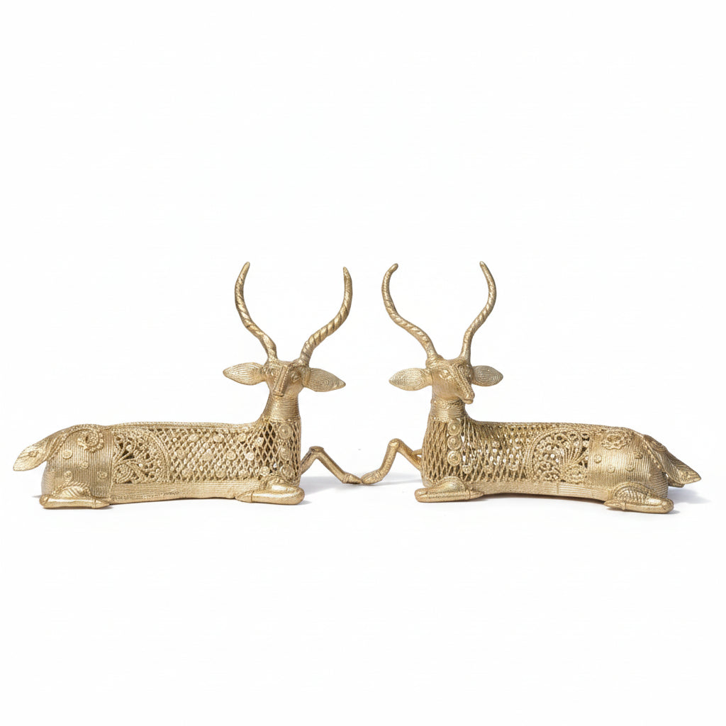 A pair of brass sculptures depicting twin deer, set against a natural background.