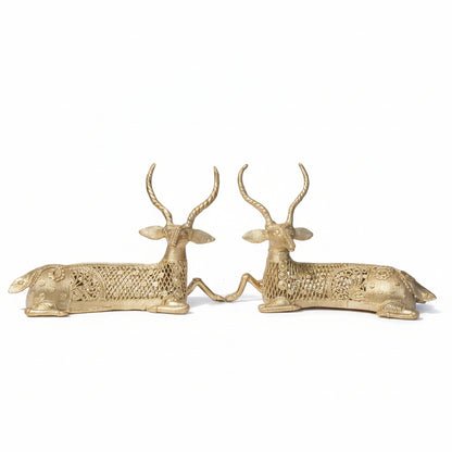 A pair of brass sculptures depicting twin deer, set against a natural background.