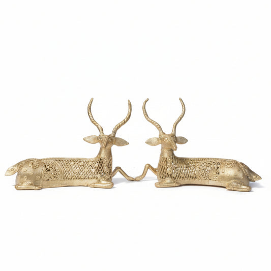 A pair of brass sculptures depicting twin deer, set against a natural background.